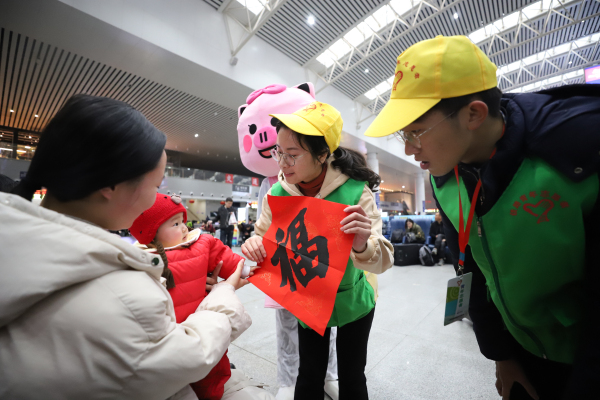 图二：1月10日，在南昌站候车厅，南昌工务段青年志愿者付映雪向小旅客送上“福”字。