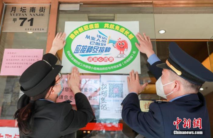 2月22日，北京市西城区市场监管局工作人员为同和居(月坛店)张贴“应接尽接”标识。截至目前，西城区已有近千家餐饮企业的员工参与了疫苗接种，部分老字号、单位食堂、连锁品牌等餐饮单位接种率超过90���饮冷链食品从业人员接种率为95���城区陆续对辖区内已完成新冠疫苗“应接尽接”的餐饮企业发放标识，并向店内已完成疫苗接种的人员发放胸牌，对近千家实现“应接尽接”的餐饮服务单位进行了公示。 中新社记者 贾天勇 摄