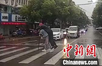 视频画面：小伙背起拄拐老人过马路。龙游交警 供图