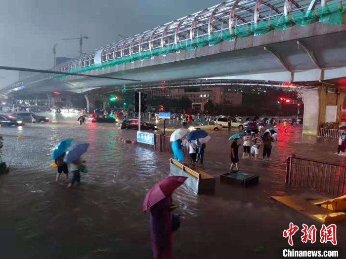 图为7月20日晚间，行人在路上趟水前行。　阚力 摄