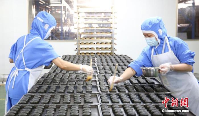 图为9月16日，广西柳州市一家烘焙生产企业的员工在给螺蛳粉月饼刷蛋液。 中新社记者 朱柳融 摄