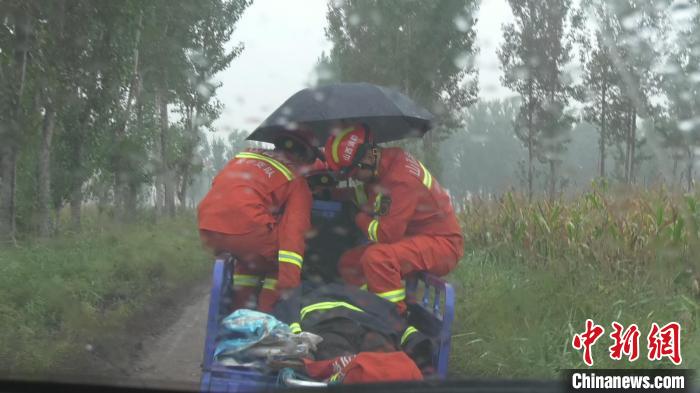 一名消防员驾驶三轮车，两名消防员轮流撑伞守护。　张烨 摄