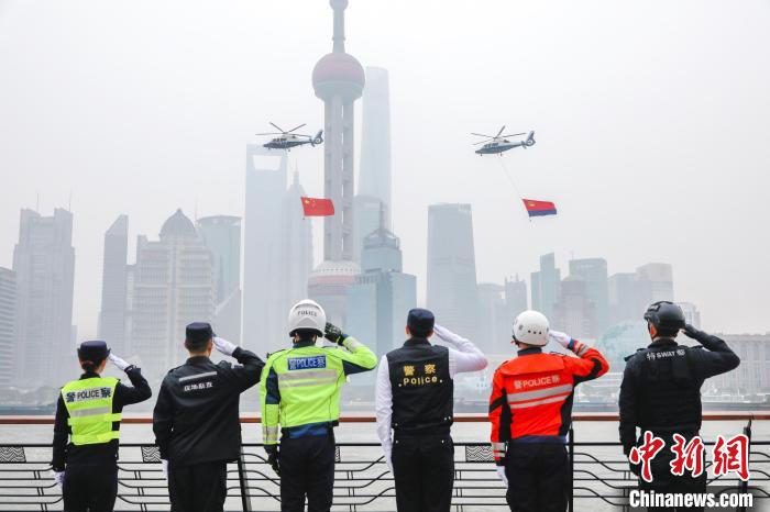 两架悬吊着巨幅国旗和警旗的警务直升机飞过外滩万国建筑群，引来黄浦江畔的游人纷纷驻足观摩。　上海警方供图