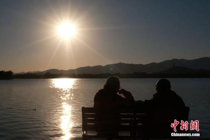 秋日的暖阳下，两位老人坐在昆明湖畔的长椅上喝着茶好不惬意。
