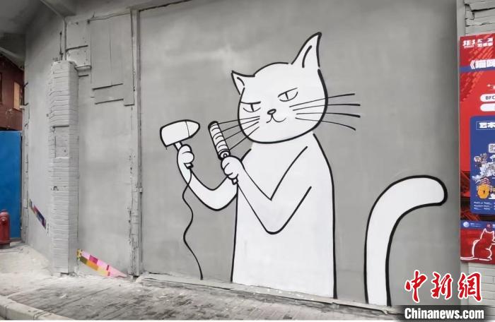 墙上漫画中，一只白猫正拿着吹风机吹着它的胡须。　郑莹莹 摄